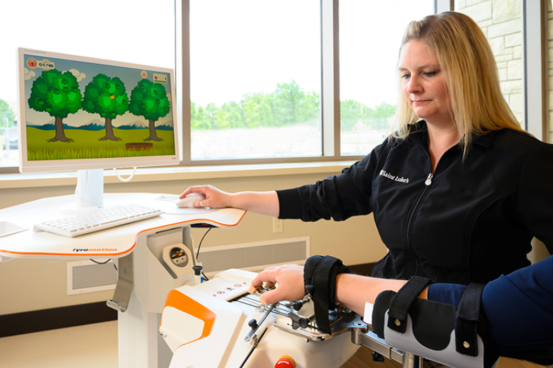 A rehabilitation worker is assisting a patient via the Tyromotion Amadeo hand/arm machine.